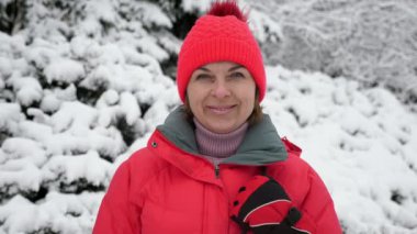 Yavaş çekimde güzel bir çam ağacında ayakta ve gülümseyen mutlu sarışın kadın pembe şapkalı ve pembe ceketli gülümseyen sarışın bir kadının neşeli portresi güneşli bir kış gününde güneşli bir ormanda duruyor.. 