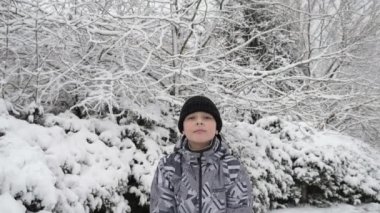 Neşeli çocuk kartopunu tutuyor ve yavaş çekimde ağaçlara fırlatıyor. Siyah şapkalı, kapüşonlu ceketli, kar tutan ve şekillendiren mutlu çocuğu görkemli bir şekilde yavaş çekimde bir kış ormanına fırlatıyor..