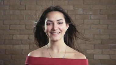 Tuğla bir stüdyoda saçlarını sallayarak gülümseyen neşeli, genç, esmer bir kız uzun, gevşek saçlı neşeli bir kadın, havada sallanıyor, neşeli bir şekilde gülümsüyor ve bir tuğla stüdyoda canlı görünüyor.. 