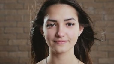 Tuğla bir stüdyoda saçlarını sallayan neşeli, genç esmer bir kız. Uzun, gevşek saçları olan, havada sallanan, neşeli, neşeli ve mutlu bir hayat süren, hayalperest bir esmer kadın.. 
