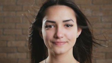 Tuğla bir stüdyoda saçlarını sallayarak gülümseyen mutlu genç esmer kız uzun, gevşek saçlı neşeli bir esmer kadın, havada sallanıyor, neşeli bir şekilde gülümsüyor ve bir tuğla stüdyoda hayatından keyif alıyor.. 