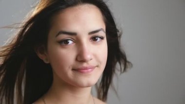 Uzun saçlarını sallayan ve neşeli bir şekilde stüdyoda duran romantik bir kız. Uzun, gevşek saçlarını sallayan ve ağır çekimde mutlu bir şekilde gülümseyen genç bir esmer kızın güzel portresi..