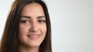 Uzun saçlı mutlu esmer kız beyaz bir stüdyoda neşeli bir şekilde ayakta duruyor ve gülümsüyor şık, genç esmer bir kızın görkemli portresi uzun sarı saçları ve parlak gözleri beyaz bir stüdyoda neşeyle duruyor ve gülümsüyor..