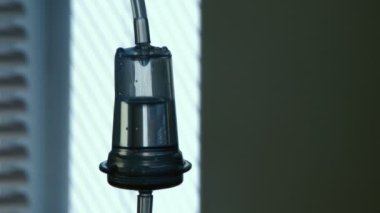 Parlak bir hastane koğuşunda tıbbi su damlatan şeffaf bir tıbbi su damlatan ve arka planda iyi ışıklandırılmış bir penceresi olan metalik bir standa yerleştirilmiş şeffaf bir plastik damlatıcının muhteşem görüntüsü..