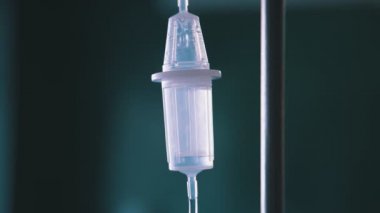 Hastane odasında mavi plastik bir damlaya damlayan sağlıklı sıvı damlaları hastane odasında bir hastaya giden plastik bir şişe ve ince bir tüple transparan bir tezgahın yakın çekimini heyecanlandırıyor. Sıvı hızlı akıyor..