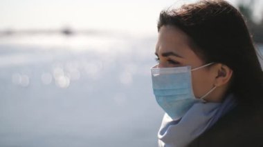 Romantik esmer güzellik, ilkbaharda parlak Dnipro nehrinin manzarasının keyfini çıkarıyor. Coronavirus 'a karşı ayakta duran ve altın günbatımında Dinyeper sularına bakan, hijyenik maske takmış güzel esmer bir kadın profiline ilham veriyor..