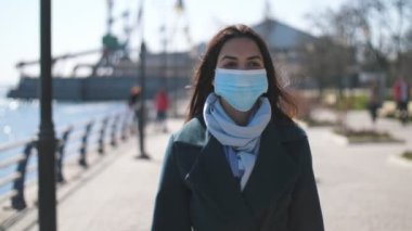 Hijyenik maske takmış güzel esmer, Dinyeper rıhtımında ağır çekimde yürüyen, zarif ceketli ve virüslere karşı hijyenik maskeli, uzun saçlı esmer bir kız..