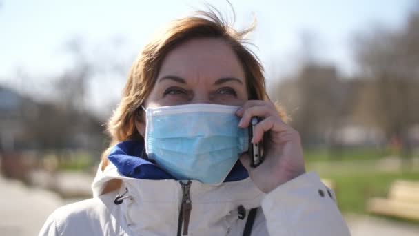 Χαρούμενη Ξανθιά Γυναίκα Μάσκα Υγιεινής Μιλάει Στο Τηλέφωνο Ένα Πάρκο — Αρχείο Βίντεο