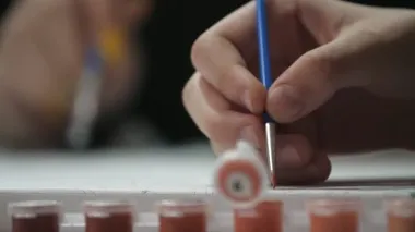 Genç bir ressamın el resmi, beyaz bir kağıtta dar bir püskülle büyük bir stüdyoda uzun mavi püsküllü bir resim yapan genç bir ressamın el resmi. İnce ve sanatsal fırça darbeleri atıyor..