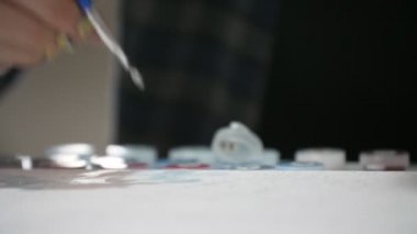 Sarı ve mavi makyajlı ruhani bir kız beyaz bir kağıtta resim yaratıyor. Sarı ve mavi makyajlı güzel bir Ukraynalı kızın büyük bir stüdyodaki beyaz bir kağıda küçük yağlı boya darbelerini yerleştiren uzun bir fırça.