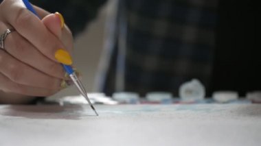 Sarı ve mavi makyajlı kadın sanatçı parmakları, Ukraynalı kadınların sarı ve mavi makyajlı ve uzun fırçalı, havadar bir stüdyodaki beyaz bir kağıda ince yağlı boya darbeleri yerleştiren Vatanseverlik portresi üzerinde bir resim oluşturuyor.