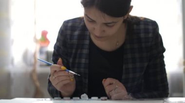 Vatansever makyajlı düşünceli bir kadın sanatçı kâğıt bir çarşafa resim çiziyor. Parlak esmer bir kızın, sarı makyajlı ve elinde mavi püsküllü bir kızın, stüdyodaki beyaz bir erkek çarşafına yağlı boya fırçası darbeleri vurduğunu gösteriyor.