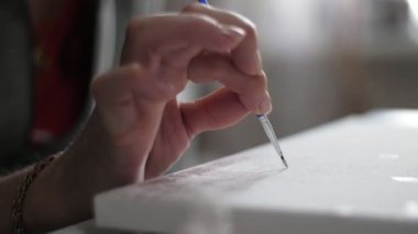 İnce püsküllü kadın parmakları ve stüdyo kâğıdının üzerine resim çizen modern makyajlı aristokrat kadın parmakları ince ve uzun bir fırça tutuyor ve stüdyodaki beyaz bir kağıt parçasına resim çiziyor.