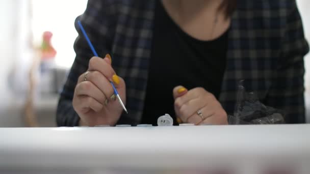 一位富有创造力的年轻女子正在画一幅画 她坐在桌子旁边 手里拿着一把稀疏的刷子 — 图库视频影像