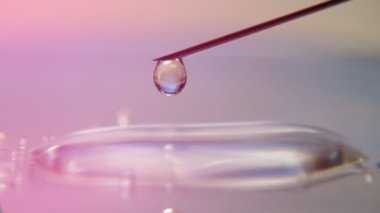 Şeffaf tıbbi sıvı damlaları pürüzsüz bir yüzey üzerinde küçük bir havuza damlıyor. Modern bir laboratuvarda, küçük bir havuza dökülen koronavirüsü test etmek için kullanılan şeffaf tıbbi sıvı akışına yakın çekim uyarısı..