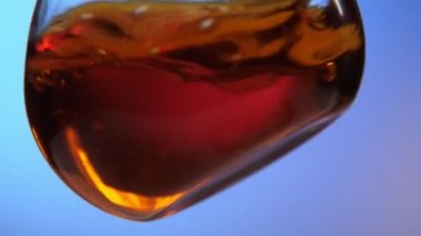 Kahverengi test sıvısı modern bir laboratuvarda büyük yuvarlak bir şişede kırmızı kandan bir karışım ve mavi arkaplan ile çağdaş bir laboratuarda dönen tıbbi sıvıyla şaşırtıcı bir şekilde sarsılır..