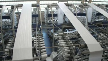 Tarım çantası üretim makineleri ve beyaz bobinlerle dolu büyük bir atölye beyaz tarım plastik çuvalları üreten büyük bir fabrika salonunun manzarası heyecan verici ve büyük torbalar için ipler yapan dönen makaralı birçok makine..