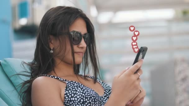 一个穿着比基尼 戴着太阳镜的漂亮姑娘坐在一个海滨度假胜地的长椅上 从社交网络中得到许多喜欢的东西 这真是浪漫的景象 用户界面动画 — 图库视频影像