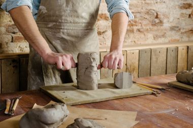 Potter, kil atölye, Seramik Sanat kavramı - erkek kesim ham kil dize kesici, closeup giymiş bir önlük, Fransız iş araçları kümesi heykel ile ahşap masa üzerinde duran adamın elleri ile