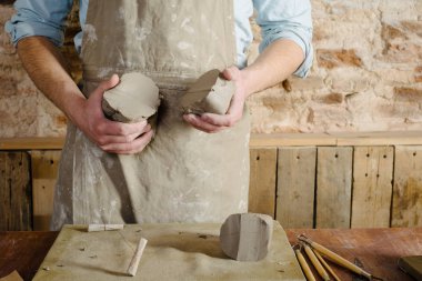 Potter, atölye, Seramik Sanat kavramı - genç esmer adam ayakta bir önlük giymiş, erkek eller yoğurmak şamot hammadde heykel araçlar kümesi ile ahşap tablo ile bir ustası