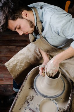 çanak çömlek, atölye, Seramik Sanat kavramı - potter's tekerlekli el ile ham kil ile çalışan adam bir erkek esmer heykeltraşlık araçlarıyla, önlük ve bir gömlek ana ahşap masa yakınındaki bir mutfak eşyaları
