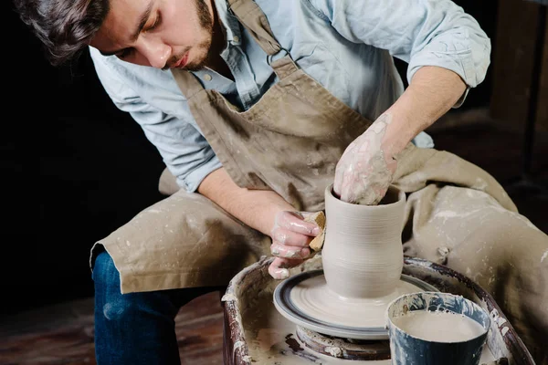 çanak çömlek, atölye, Seramik Sanat kavramı - potter's tekerlekli el ile ham kil ile çalışan adam bir erkek esmer heykeltraşlık araçlarıyla, önlük ve bir gömlek ana ahşap masa yakınındaki bir mutfak eşyaları