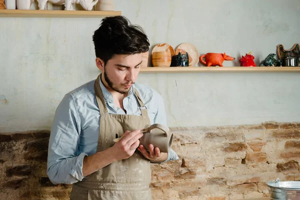 Potter, atölye, Seramik Sanat kavramı - holding Fransız Kupası ve ürün, erkek usta bir lekeli kil önlük giymiş genç dikkatle inceliyor, Usta'nın ellerini tutarak çiğ sürahi