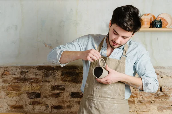 Potter, atölye, Seramik Sanat kavramı - holding Fransız Kupası ve ürün, erkek usta bir lekeli kil önlük giymiş genç dikkatle inceliyor, Usta'nın ellerini tutarak çiğ sürahi