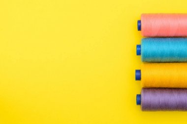 çok renkli iplik bobinleri bir boşluk ortasında bir yazıt altında sarı zemin üzerine. Dikiş üretim kavramı. Üstten Görünüm, düz Lay.