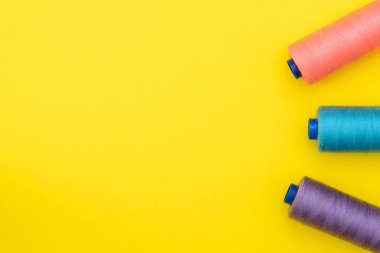 çok renkli iplik bobinleri bir boşluk ortasında bir yazıt altında sarı zemin üzerine. Dikiş üretim kavramı. Üstten Görünüm, düz Lay.