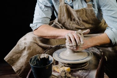 çanak çömlek, atölye, Seramik Sanat kavramı - potter's tekerlekli el ile ham kil ile çalışan adam bir erkek esmer heykeltraşlık araçlarıyla, önlük ve bir gömlek ana ahşap masa yakınındaki bir mutfak eşyaları