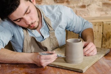 Potter, atölye, Seramik Sanat kavramı - holding Fransız Kupası ve ürün, erkek usta bir lekeli kil önlük giymiş genç dikkatle inceliyor, Usta'nın ellerini tutarak çiğ sürahi