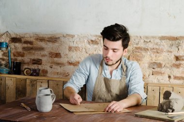 gülümseyen yakışıklı genç Meksikalı potter seramik kağıt üzerinde çizimler yapar. el işi, küçük işletme, hobi iş kavramı. 