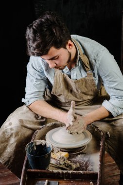 çanak çömlek, atölye, Seramik Sanat kavramı - potter's tekerlekli el ile ham kil ile çalışan adam bir erkek esmer heykeltraşlık araçlarıyla, önlük ve bir gömlek ana ahşap masa yakınındaki bir mutfak eşyaları
