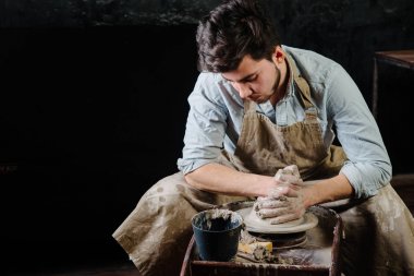 çanak çömlek, atölye, Seramik Sanat kavramı - potter's tekerlekli el ile ham kil ile çalışan adam bir erkek esmer heykeltraşlık araçlarıyla, önlük ve bir gömlek ana ahşap masa yakınındaki bir mutfak eşyaları
