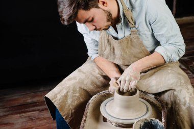 çanak çömlek, atölye, Seramik Sanat kavramı - potter's tekerlekli el ile ham kil ile çalışan adam bir erkek esmer heykeltraşlık araçlarıyla, önlük ve bir gömlek ana ahşap masa yakınındaki bir mutfak eşyaları