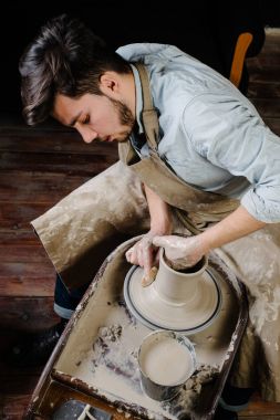 çanak çömlek, atölye, Seramik Sanat kavramı - potter's tekerlekli el ile ham kil ile çalışan adam bir erkek esmer heykeltraşlık araçlarıyla, önlük ve bir gömlek ana ahşap masa yakınındaki bir mutfak eşyaları