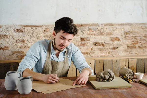 Le beau jeune potier mexicain souriant fait des croquis de céramique sur le papier. concept de petite entreprise, artisanal, travail de passe-temps . — Photo