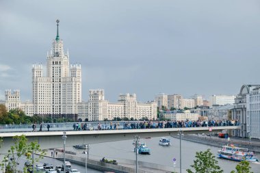 Moskova, Rusya - Ağustos 2019: Park Zaryadye. İnsanların üzerinde yürüdüğü yüzen bir köprü. Nehrin üzerinde yüzen köprünün altından eğlence tekneleri geçiyor. Stalin 'in Kotelnicheskaya seti üzerindeki gökdeleni.