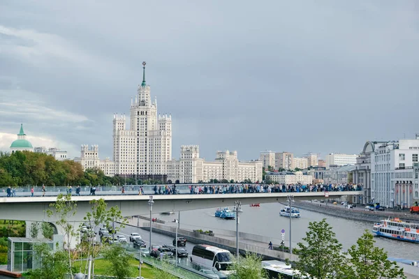 俄罗斯莫斯科- 2019年8月：Park Zaryadye 。 人们走过的浮桥。 游船在河上的浮桥下航行. 斯大林在Kotelnicheskaya堤岸上的摩天大楼. — 图库照片