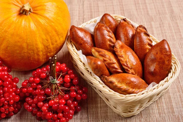 Geleneksel Rus usulü pirozhki turtaları sepette. Altın hamurlu mayalı çörekler. Sonbahar natürmort, balkabağı ve viburnum