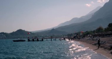 Dalgalar deniz sahil şeridi ile insanlar ve yaz gününde iskeleye demirlemiş teknelerin, görünümünü