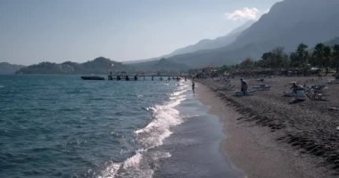 Dalgalar deniz sahil şeridi ile insanlar ve yaz gününde iskeleye demirlemiş teknelerin, görünümünü