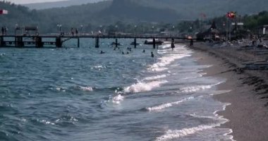 Dalgalar deniz sahil şeridi ile insanlar ve yaz gününde iskeleye demirlemiş teknelerin, görünümünü
