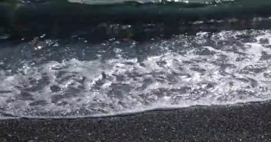 Parlak ve deniz yüzeyi parıldayan bir sahil şeridi üzerinde inişli çıkışlı dalgalar