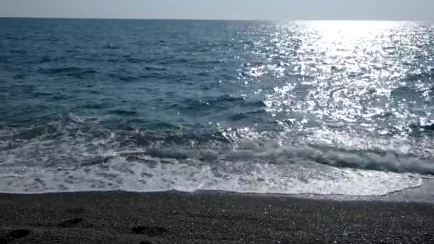 Parlak ve deniz yüzeyi parıldayan bir sahil şeridi üzerinde inişli çıkışlı dalgalar — Stok video