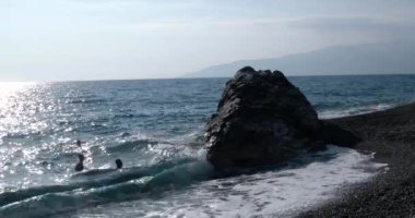 Dalgalar deniz sahil şeridi ile insanlar yüzme ile büyük Rock, haddelenmiş görünümünü