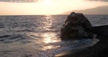 Dalgalar deniz sahil şeridi ile büyük Rock, günbatımında haddelenmiş görünümünü