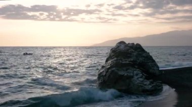 Dalgalar deniz sahil şeridi ile büyük Rock, günbatımında haddelenmiş görünümünü