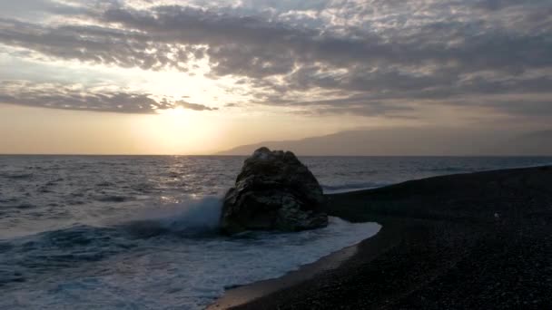 Vista de las olas rodadas en la línea de la costa del mar con enorme roca al atardecer — Vídeo de stock